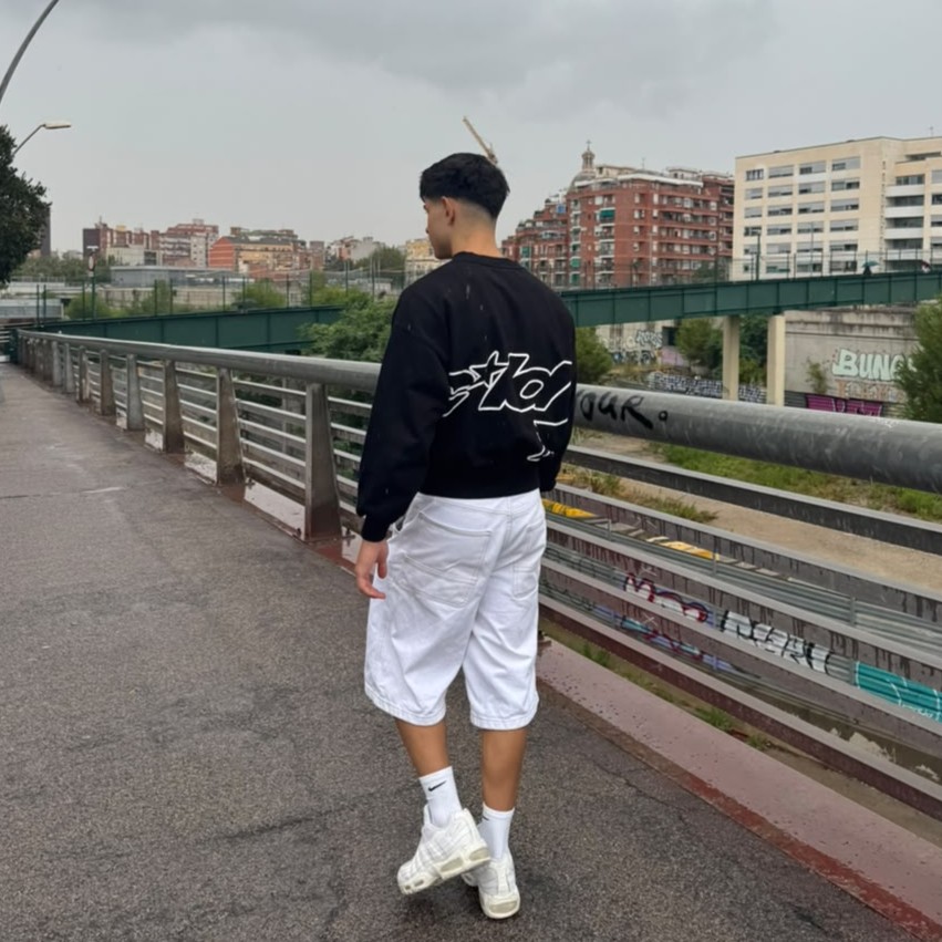 Samuel de espaldas caminando por un puente urbano bajo un cielo gris